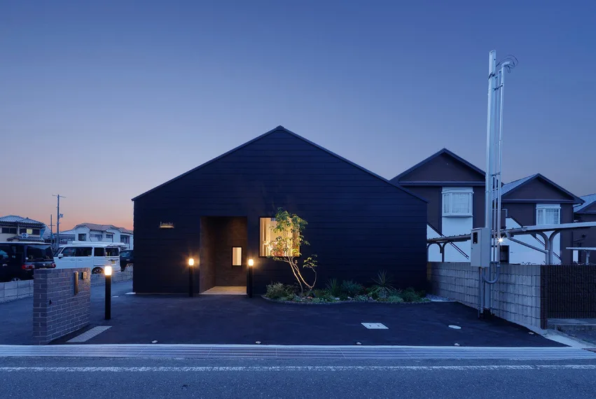 夕暮れに明かりがともる、黒い板張りの建物外観